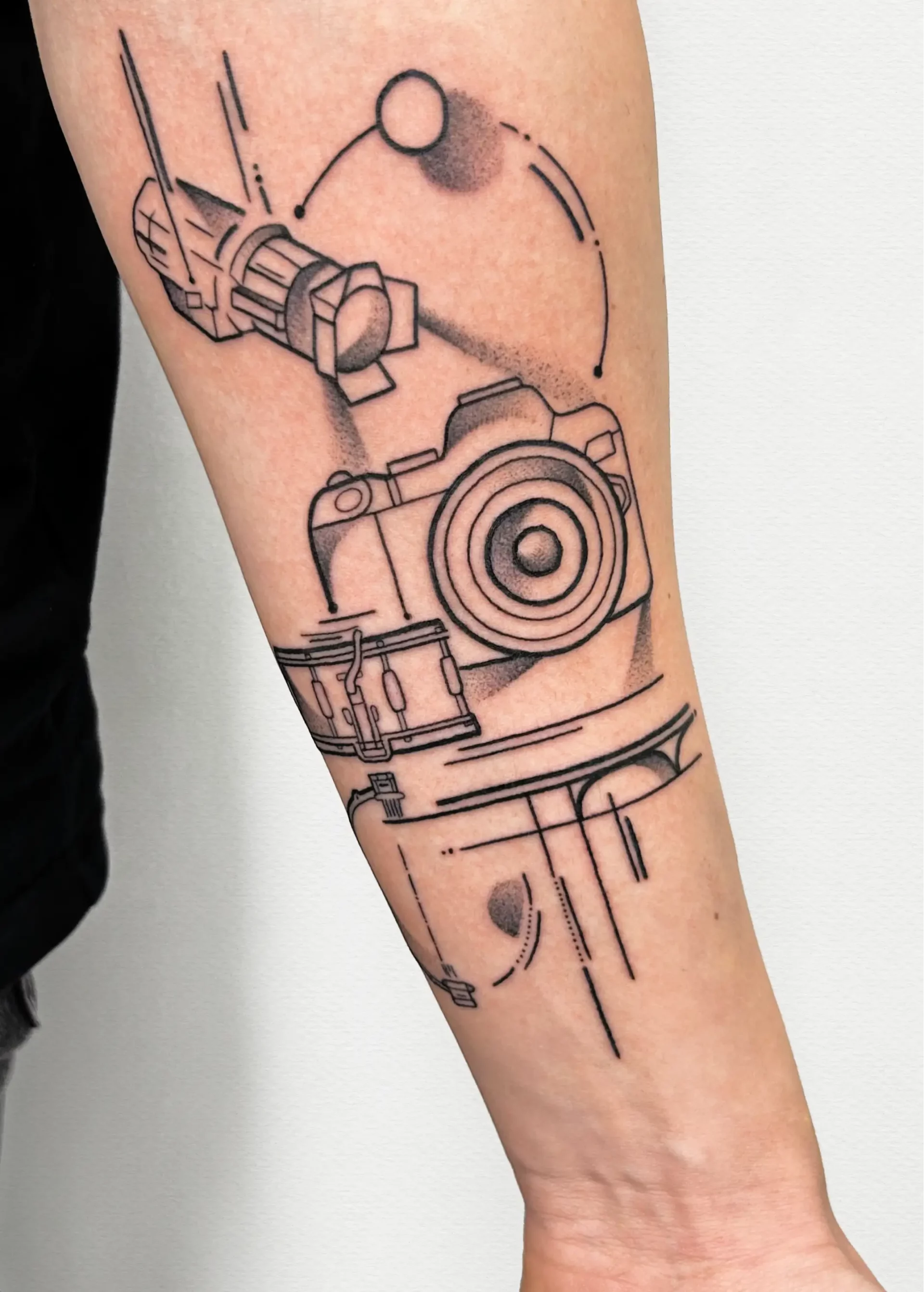 black fineline tattoo of a camera on forearm