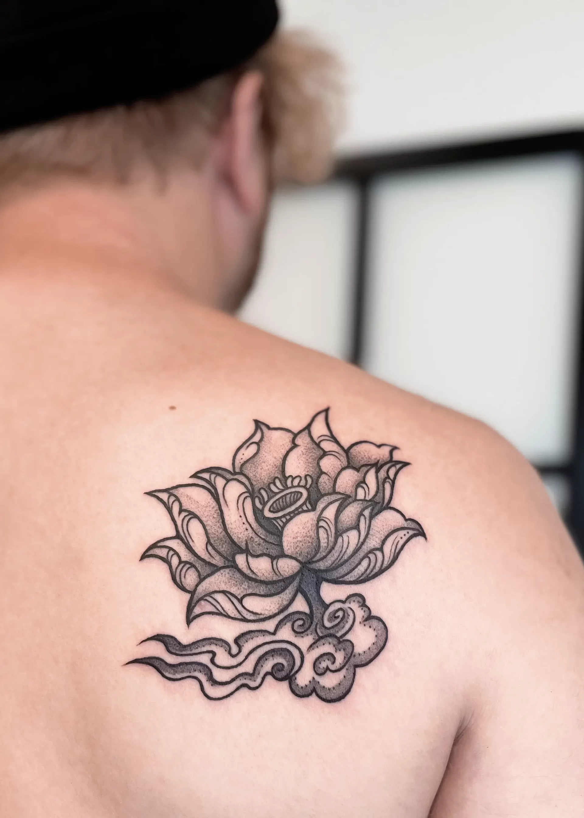 A man sporting a black and white tattoo of a lotus flower on his right shoulder